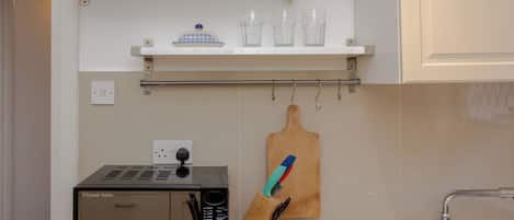 A kitchen with a microwave, a knife block, and a shelf with glassware.
