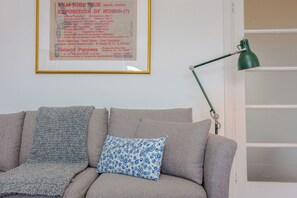 A room with a grey sofa, a patterned pillow, a framed poster on the wall, and a green desk lamp. - Contemporary 2BD Flat in Bayswater, West London (London)