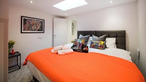 A modern bedroom with a large bed, a headboard, a framed artwork on the wall, and a small bedside table with a vase of flowers. - Windmill House Apartment 2 (Lytham Saint Annes)