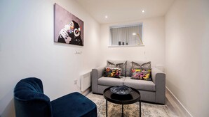 A modern living room with a grey sofa, a blue armchair, and a small black table with a glass object. - Windmill House Apartment 2 (Lytham Saint Annes)