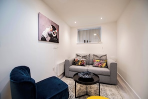Una sala de estar moderna con un sofá gris, un sillón azul y una pequeña mesa negra con un objeto de vidrio.