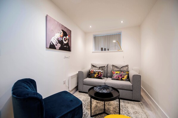 A modern living room with a grey sofa, a blue armchair, and a small black table with a glass object.
