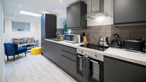 A modern kitchen with a built-in oven, microwave, and toaster. There is a dining area with a blue chair and a yellow ottoman. - Windmill House Apartment 2 (Lytham Saint Annes)