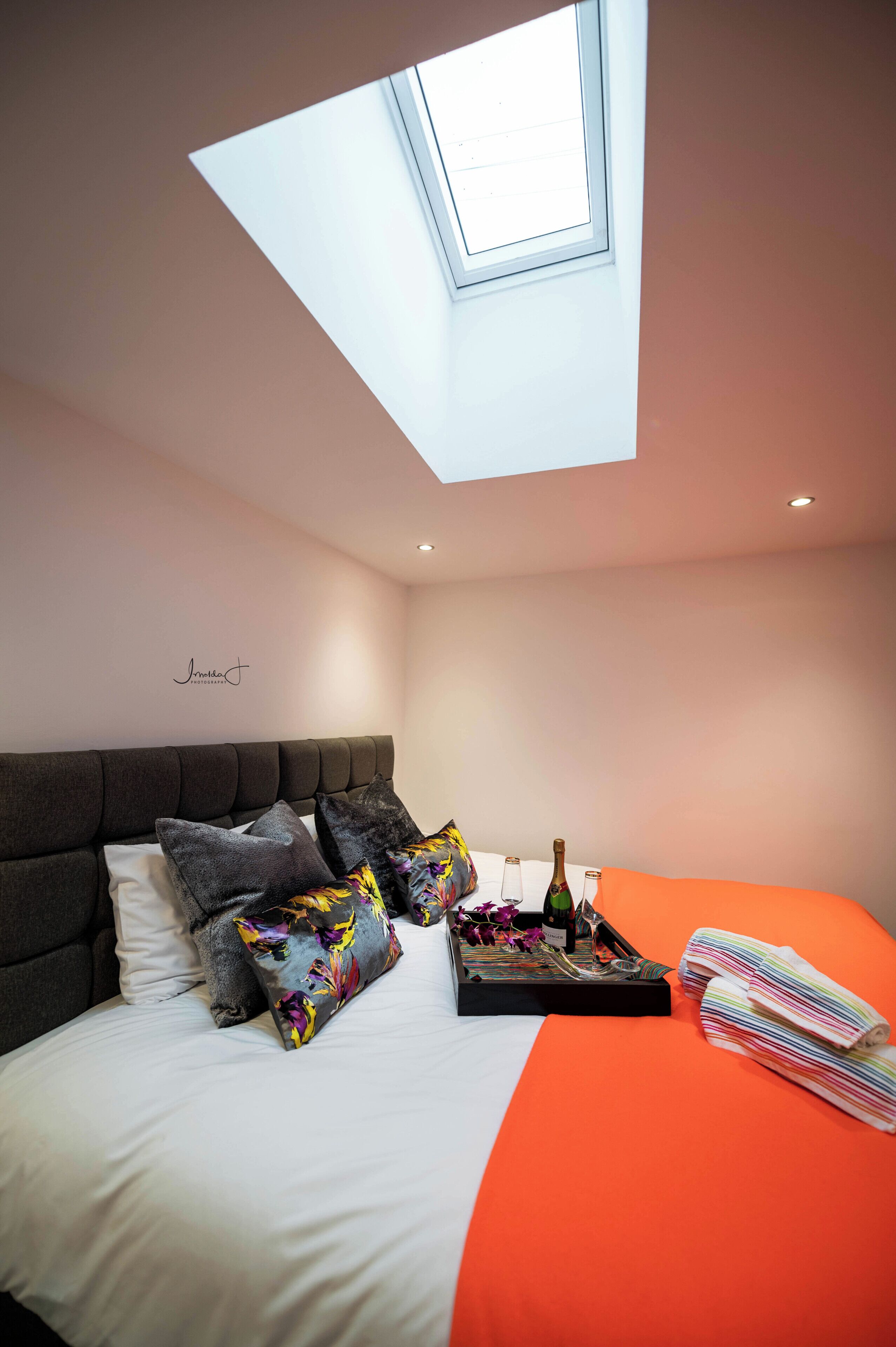 A bedroom with a bed, pillows, a tray with flowers, a bottle, and a towel.