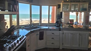 Eine Küche mit Blick auf den Strand, inklusive Herd, Schränken und Kaffeemaschine.