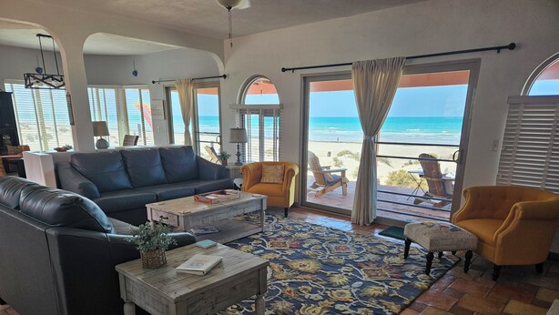 Ein Wohnzimmer mit einer Couch, Sesseln, einem Couchtisch und Blick auf den Strand.