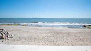 A beach with a wooden staircase leading down to the water, a clear sky, and calm waves.