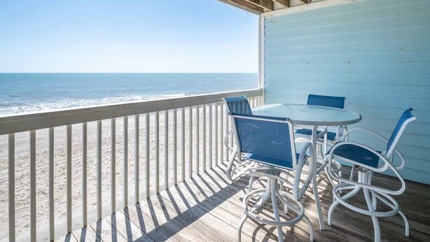 A balcony with a view of the ocean, a round table, and two chairs.