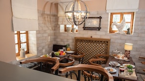 A dining area with a brick wall, wooden chairs, a chandelier, and a window with a rooster decoration.