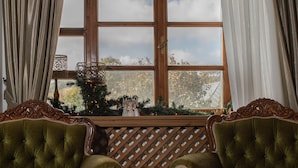 A room with two green upholstered chairs, a wooden table, and a window with curtains.