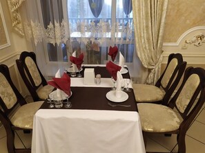 A dining table set for four with white tablecloth, red napkins, and silverware.