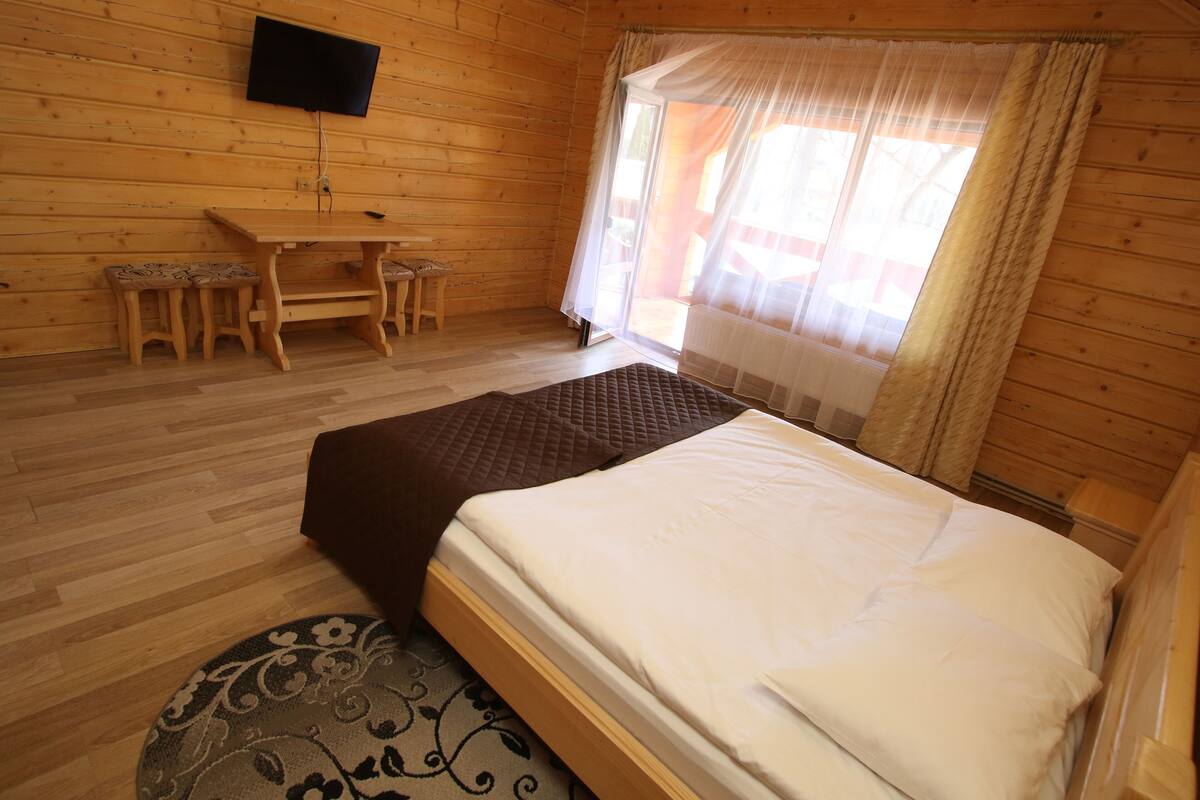 A wooden room with a bed, a desk, and a TV.