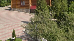 A wooden house with a steep roof, surrounded by a paved driveway and a small garden with a birdbath.