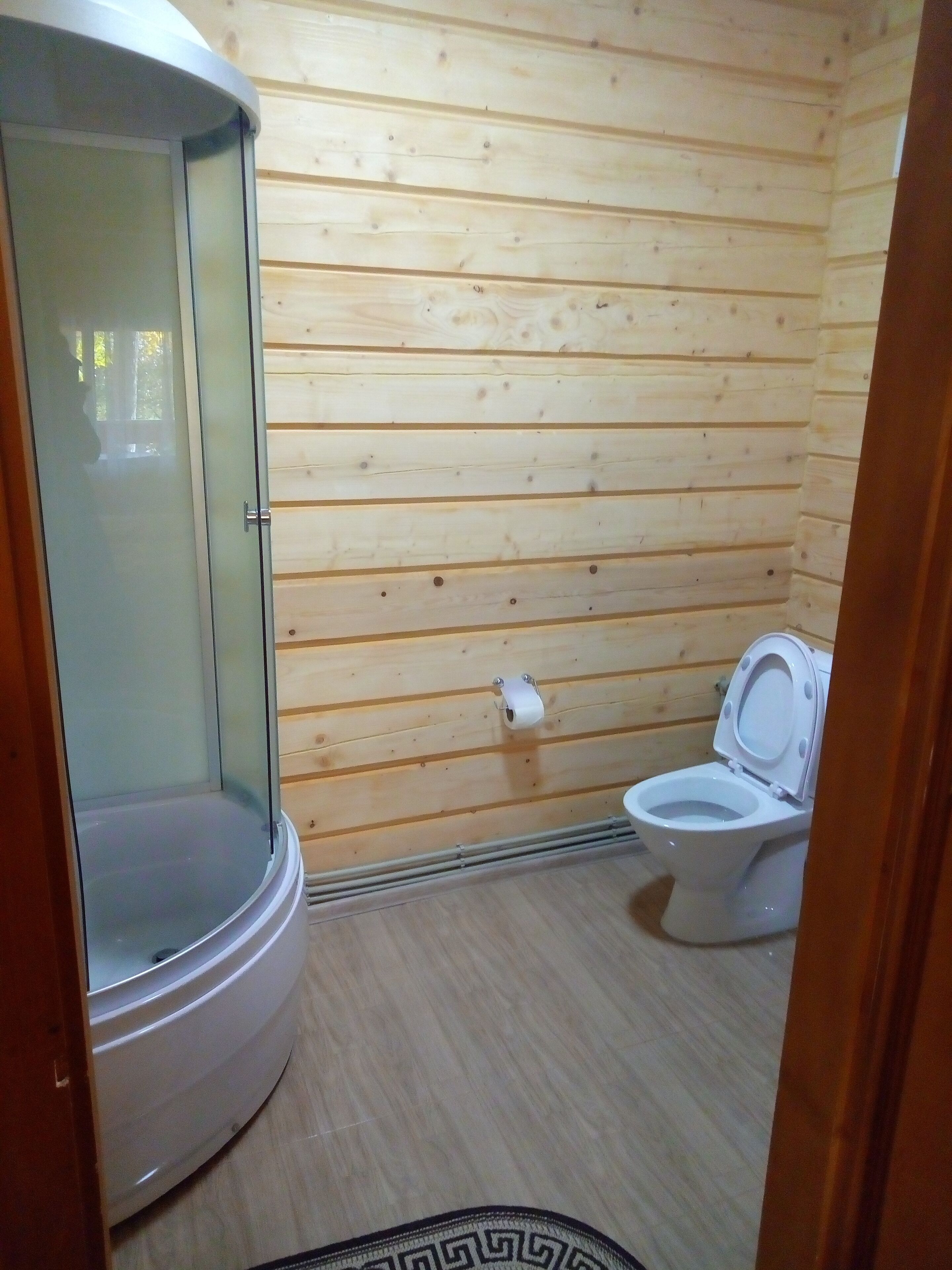 Un baño pequeño y funcional con paredes de madera, cabina de ducha de vidrio y un inodoro blanco.