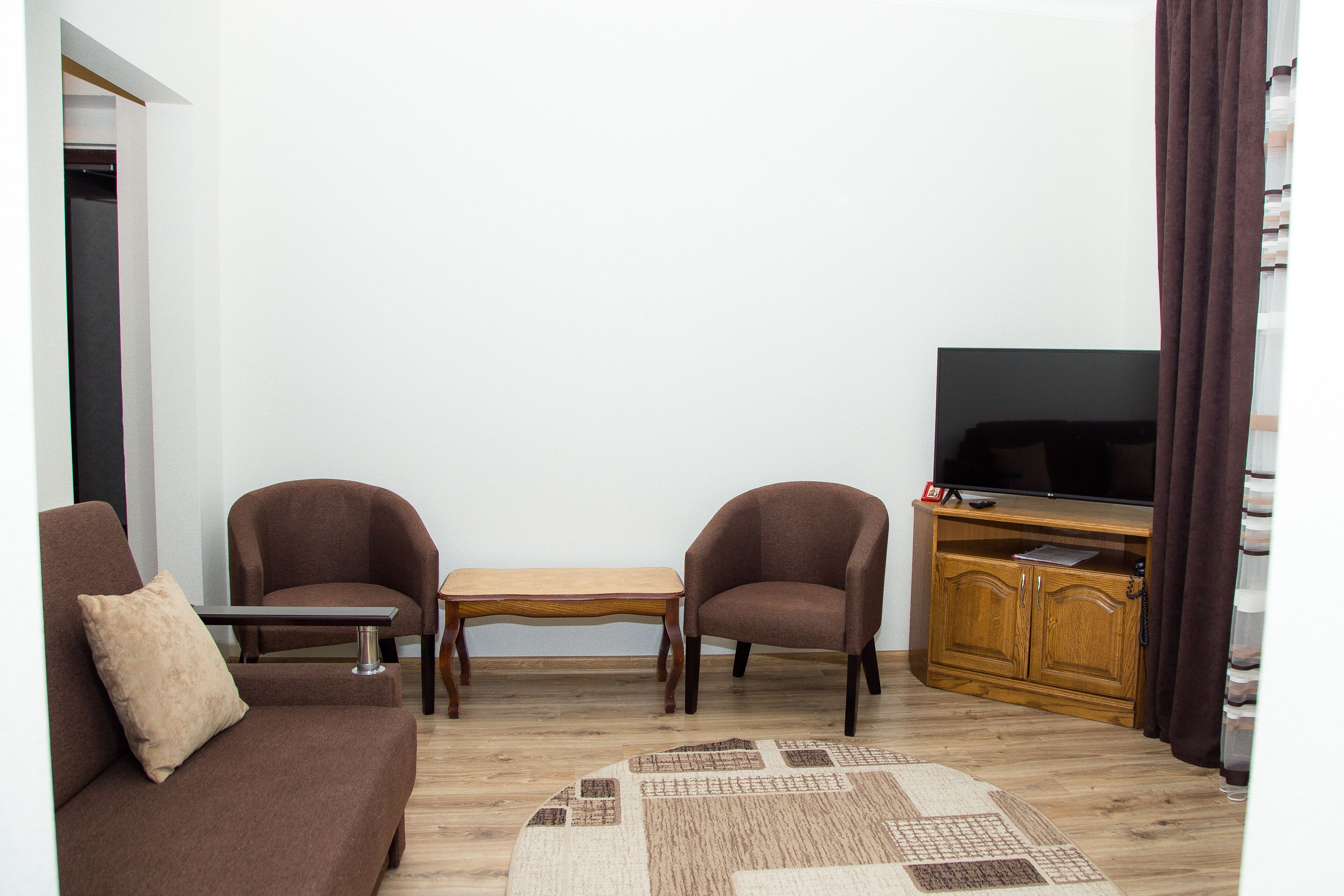A living room with a brown sofa, two armchairs, a wooden coffee table, a TV on a wooden stand, and a patterned rug.