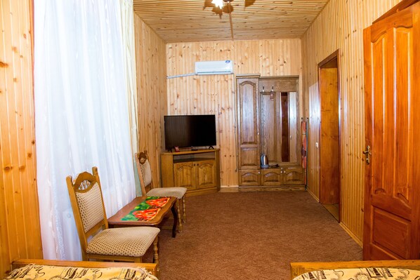 A wooden-paneled room with a television on a wooden cabinet, a dining table with chairs, and a wardrobe.