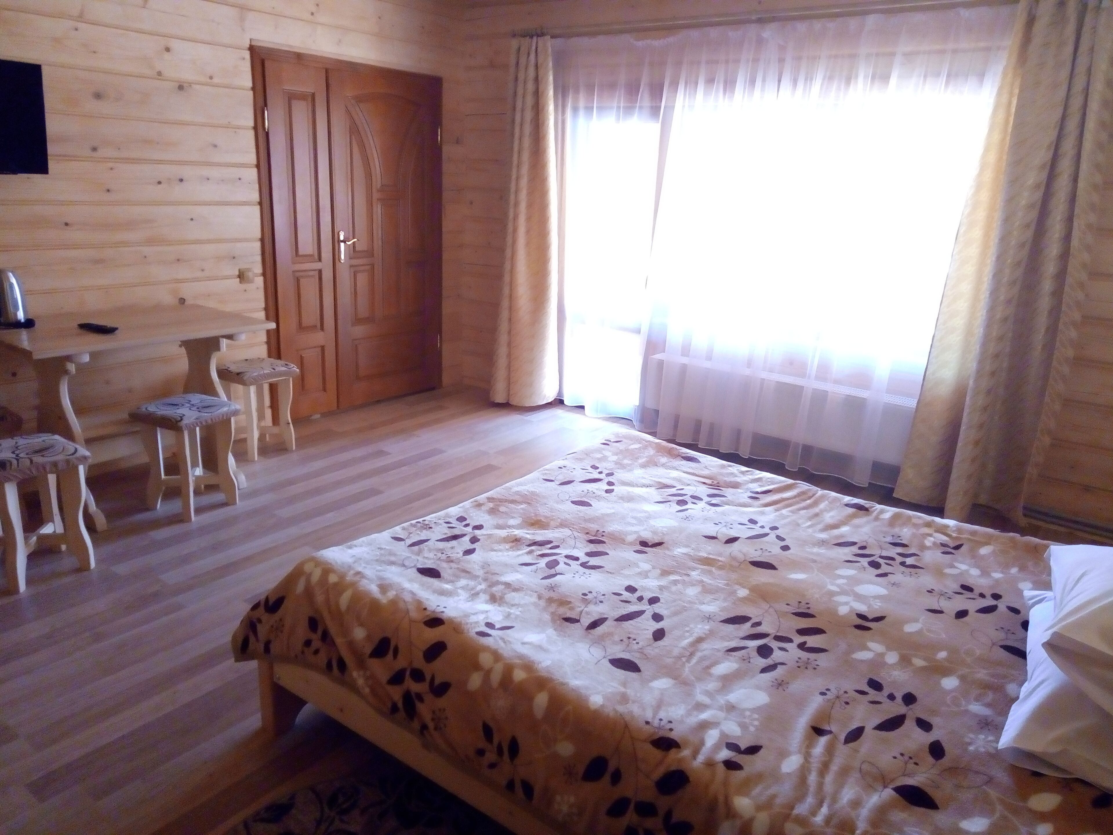 A wooden room with a bed, two chairs, a table, and a door.