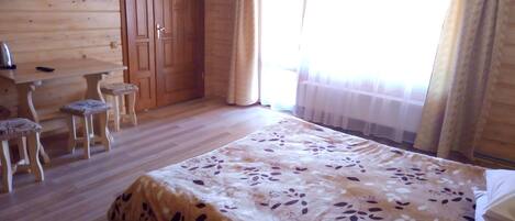 A wooden room with a bed, two chairs, a table, and a door.