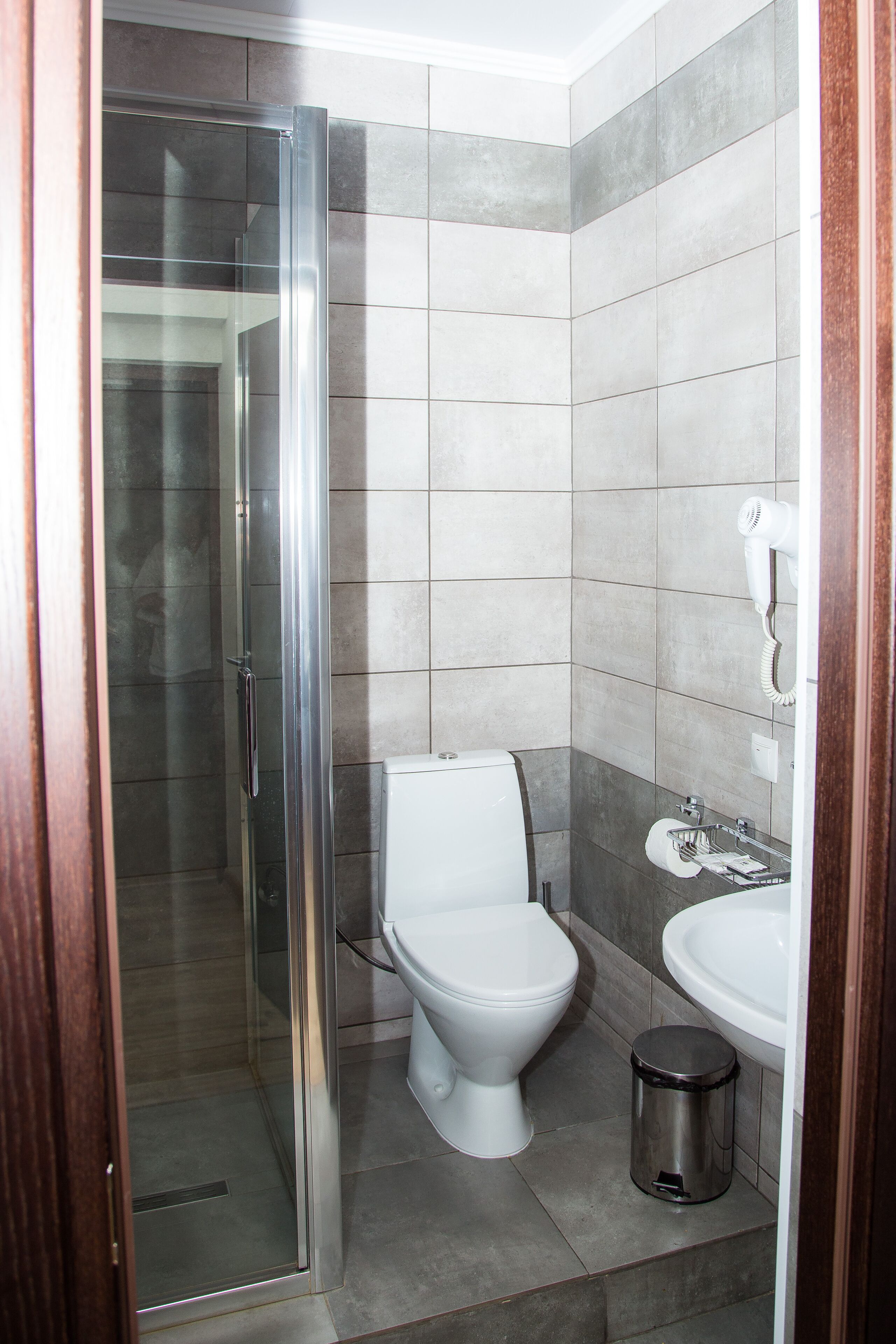 A bathroom with a glass shower enclosure, a toilet, a sink, and a trash can.