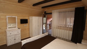 A wooden-paneled bedroom with a bed, a dresser, a television, and a sliding glass door to a balcony.