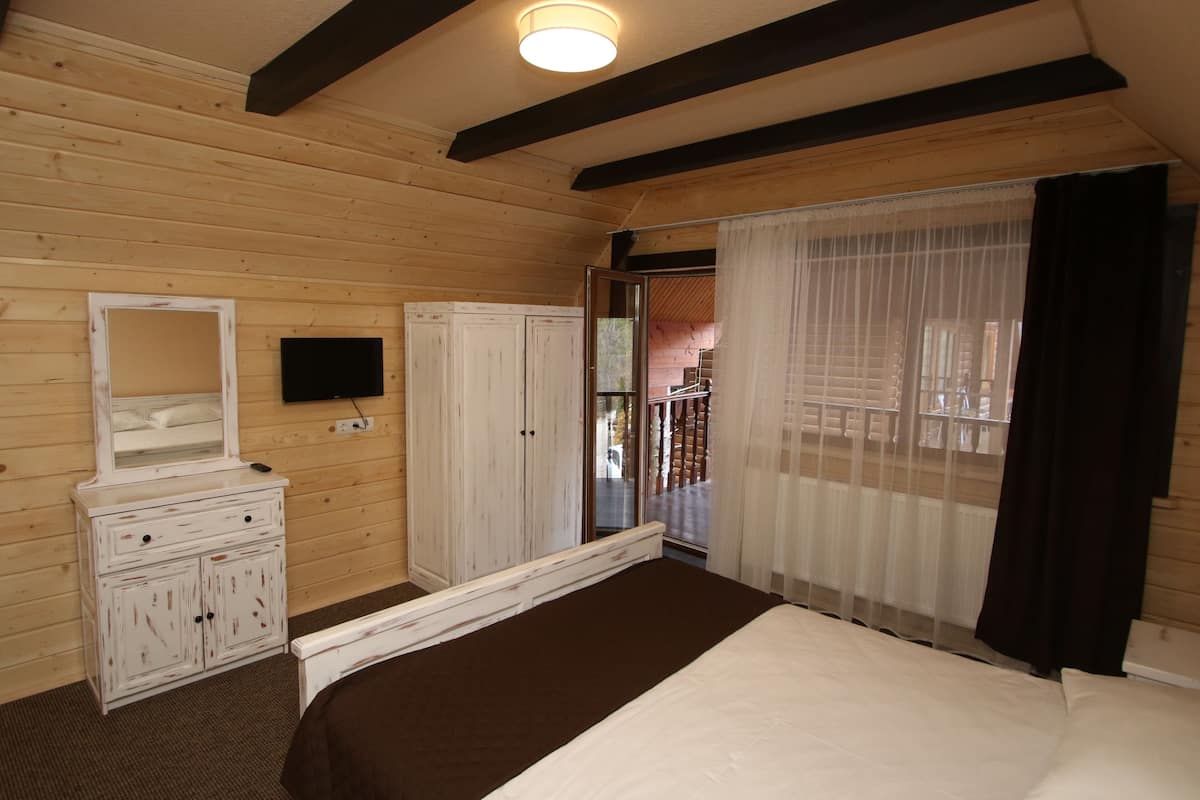 A wooden-paneled bedroom with a bed, a dresser, a television, and a sliding glass door to a balcony.