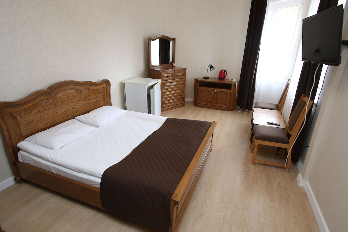 A bedroom with a wooden bed, a dresser, a mirror, a desk with a chair, and a television.