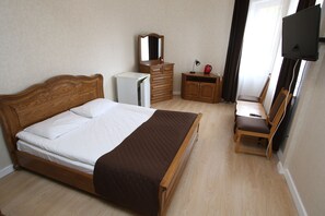 A bedroom with a wooden bed, a dresser, a mirror, a desk with a chair, and a television.