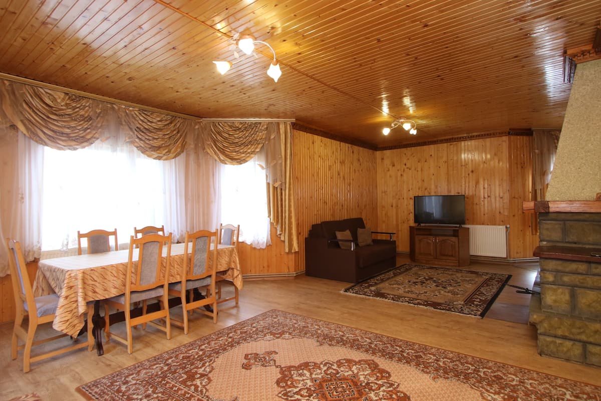 A wooden-paneled room with a dining table, chairs, a sofa, a television, and a fireplace.