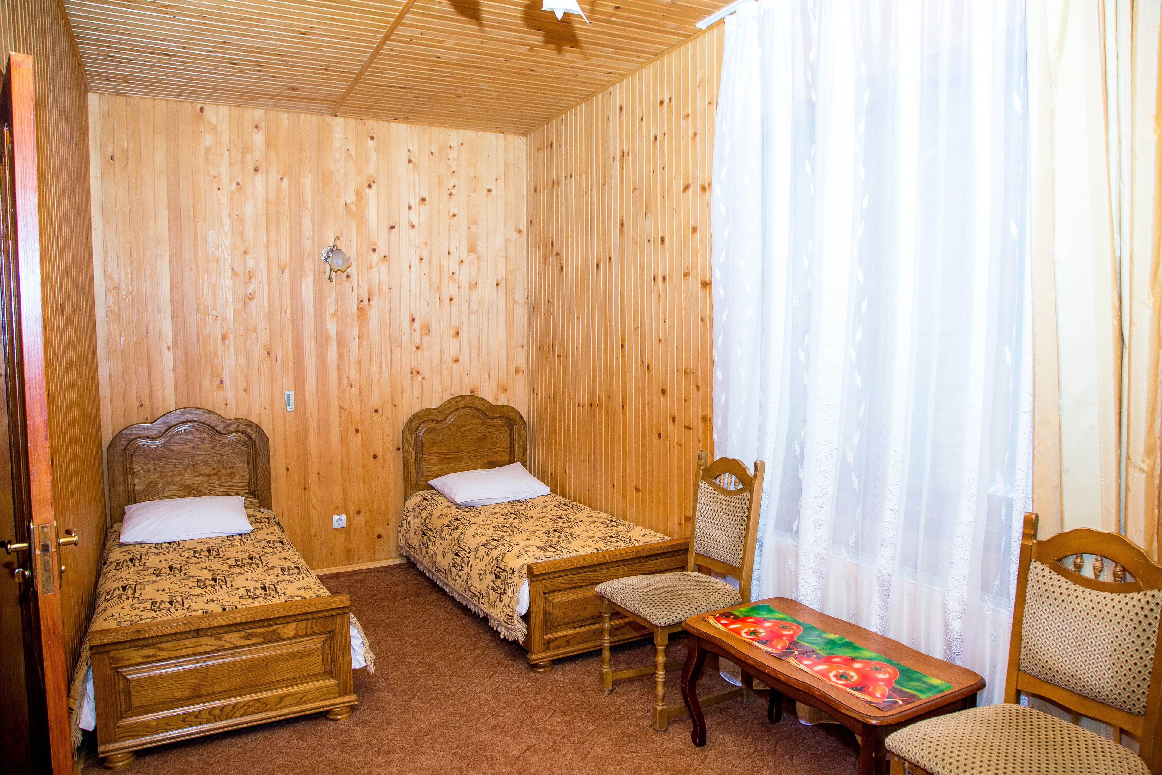 A wooden room with two beds, a chair, and a table.