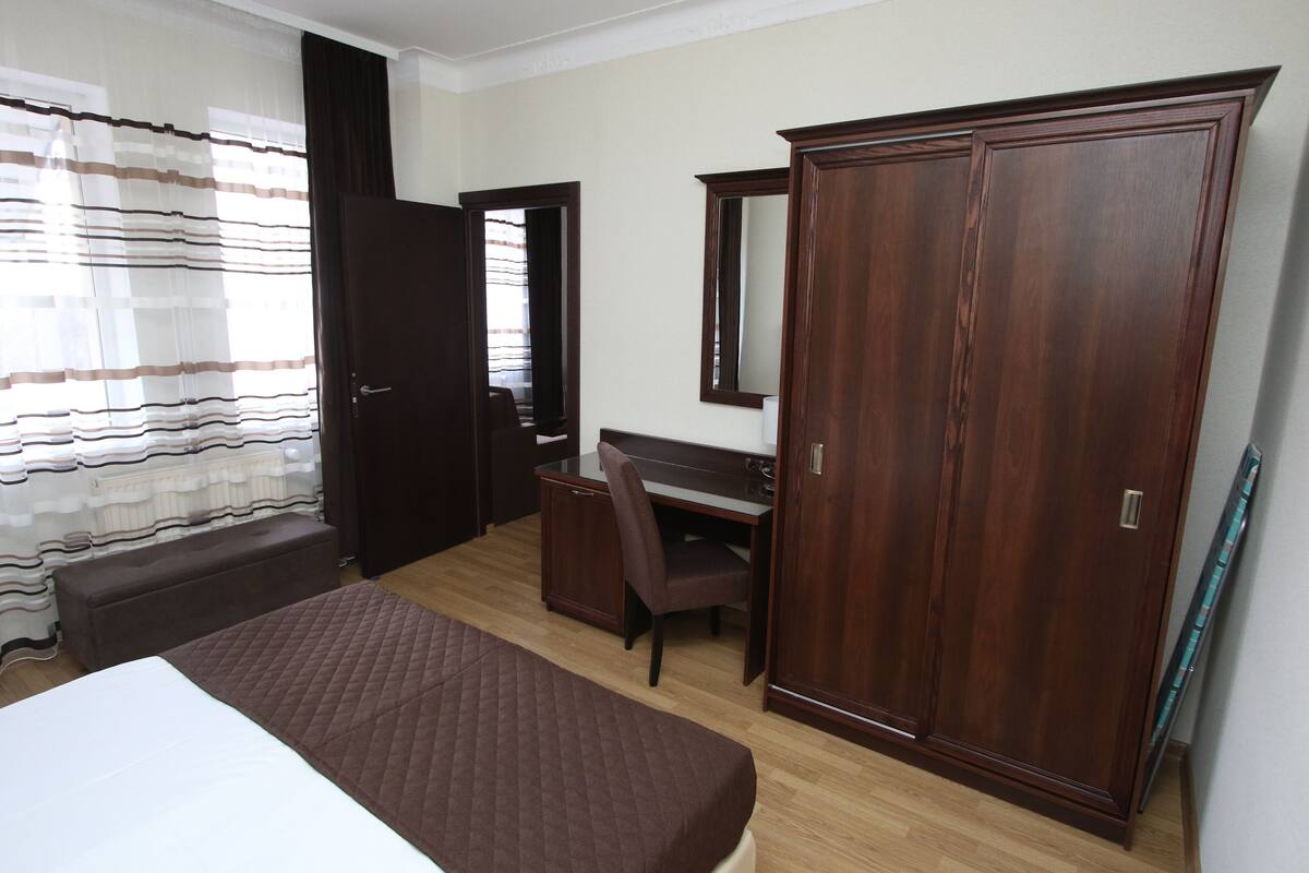 A hotel room with a bed, a desk, a chair, a wardrobe, and a mirror.