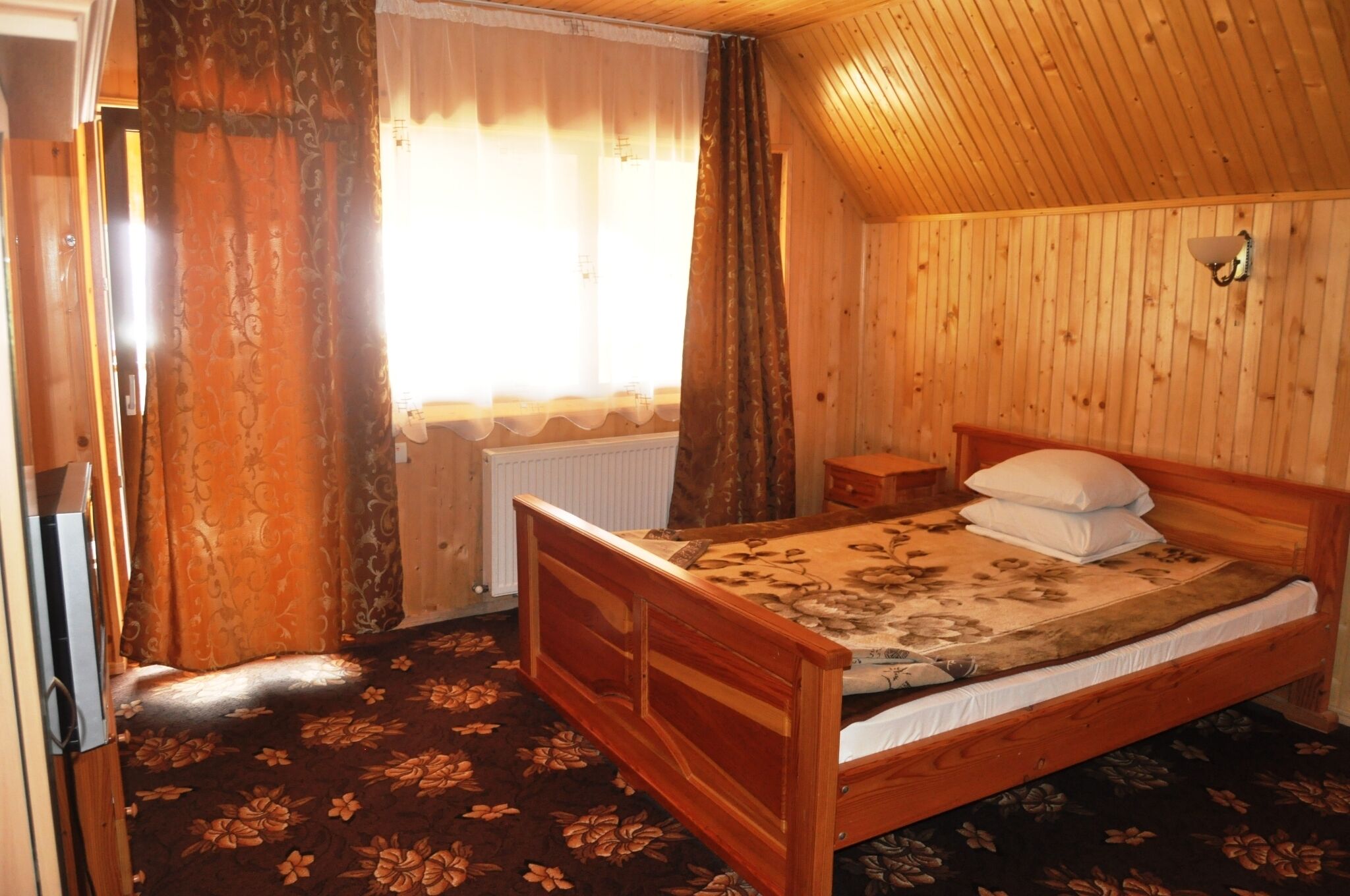 Una habitación con paneles de madera, una cama, un radiador y una ventana con cortinas.