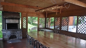 A covered outdoor dining area with a stone fireplace, wooden tables, and metal chairs.