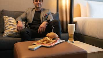 Un hombre sentado en un sofá con una hamburguesa y papas fritas sobre la mesa frente a él.