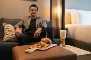 Un hombre sentado en un sofá con una hamburguesa y papas fritas sobre la mesa frente a él.