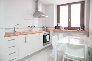 A kitchen with white cabinets, a stainless steel sink, an oven, a microwave, and a window with wooden shutters. - Apartamento Barrocal by Cadiz Time (Cádiz)