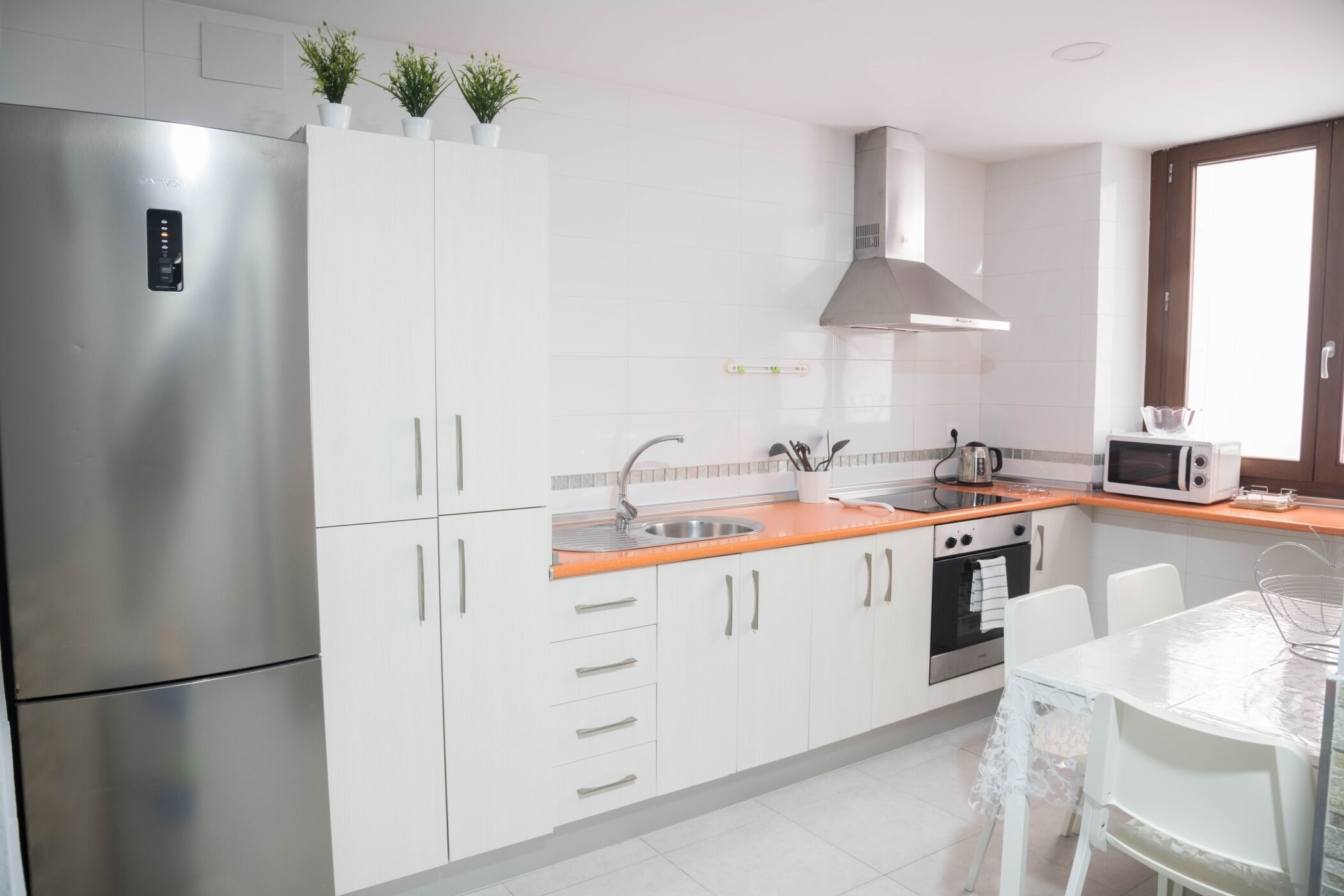 Een moderne keuken met witte kasten, roestvrijstalen apparatuur en een raam voor natuurlijk licht.