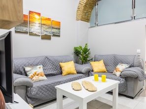A modern living room with a grey sofa, yellow cushions, a white coffee table, and a large window with a view of the sea.