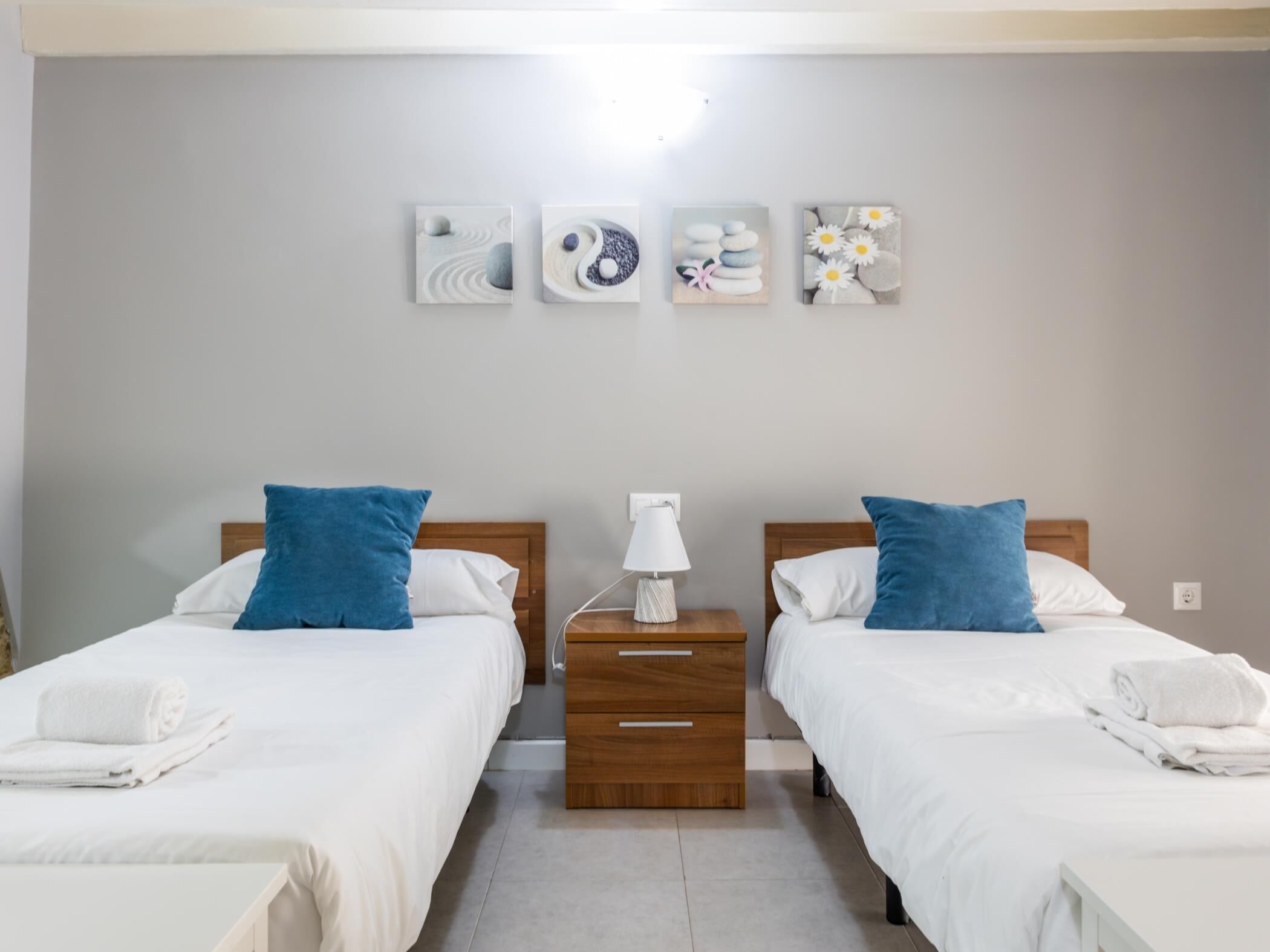Hotellihuone, jossa on kaksi sänkyä, yöpöytä ja seinätaideteos.