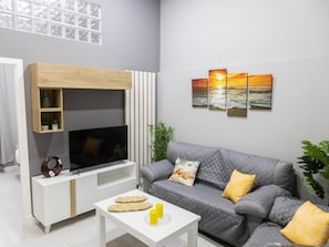 A modern living room with a flat-screen TV, a grey sofa, a white coffee table, and a wall-mounted shelf. - Apartamento Barrocal by Cadiz Time (Cádiz)