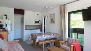 A compact living space with a kitchenette, a dining table, a sofa, and a window with a view of greenery. - Croisette / Dorons / 6 places (LES MENUIRES)