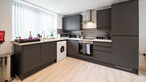 Een moderne keuken met donkere kastjes, een ingebouwde wasmachine, een magnetron en een fornuis.