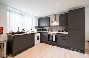 A modern kitchen with dark cabinetry, a built-in washing machine, a microwave, and a stove.