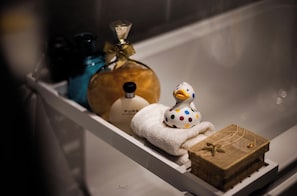 A bathroom with a bathtub containing a duck-shaped soap dispenser, a bottle of Pure shampoo, and a small wooden box.