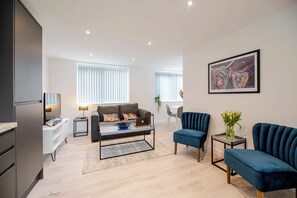 A modern living room with a sofa, a coffee table, and a blue armchair. There is a painting on the wall and a plant on a side table.