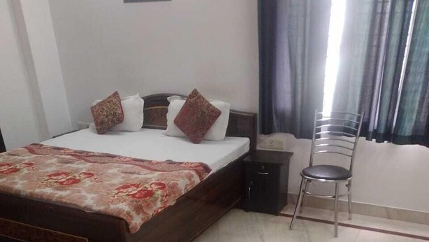 A bedroom with a bed, a nightstand, a chair, and a window with curtains. - ADB Rooms Knights Inn (New Delhi)