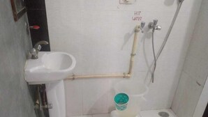 A small bathroom with a white sink, a toilet, and a shower. - ADB Rooms Knights Inn (New Delhi)