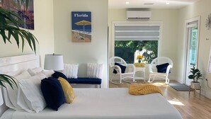 A modern bedroom with a large bed, white bedding, and a blue rug. There is a painting of Florida on the wall, a white chair, and a small table with a vase of flowers. - Miami Skyline Luxury Suite With Private Patio and Parking . (Miami)
