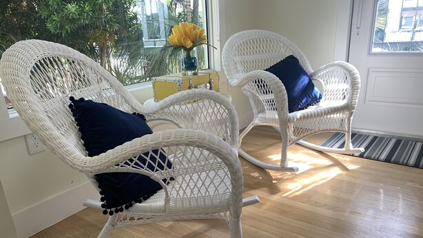 Two white wicker rocking chairs with dark blue cushions, positioned on a wooden floor near a window with a view of greenery outside. - Miami Skyline Luxury Suite With Private Patio and Parking . (Miami)