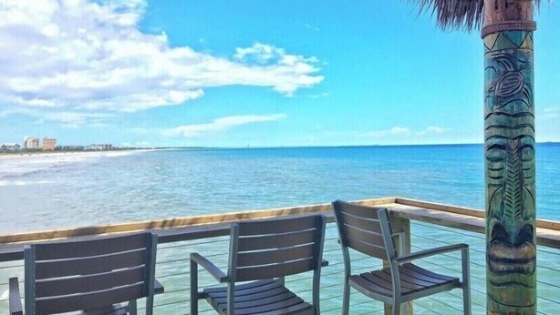 Una terraza de madera con dos sillas que dan a una playa.
