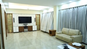 A spacious living room with a flat-screen TV mounted on the wall, a beige sofa, a coffee table, and a red rug. - Republic Hotel (Patna)
